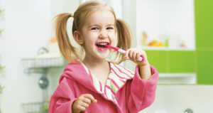 a young child in pigtails brushing her teeth and smiling