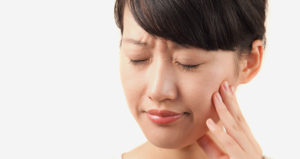 Asian woman puts hand on jaw due to tooth pain
